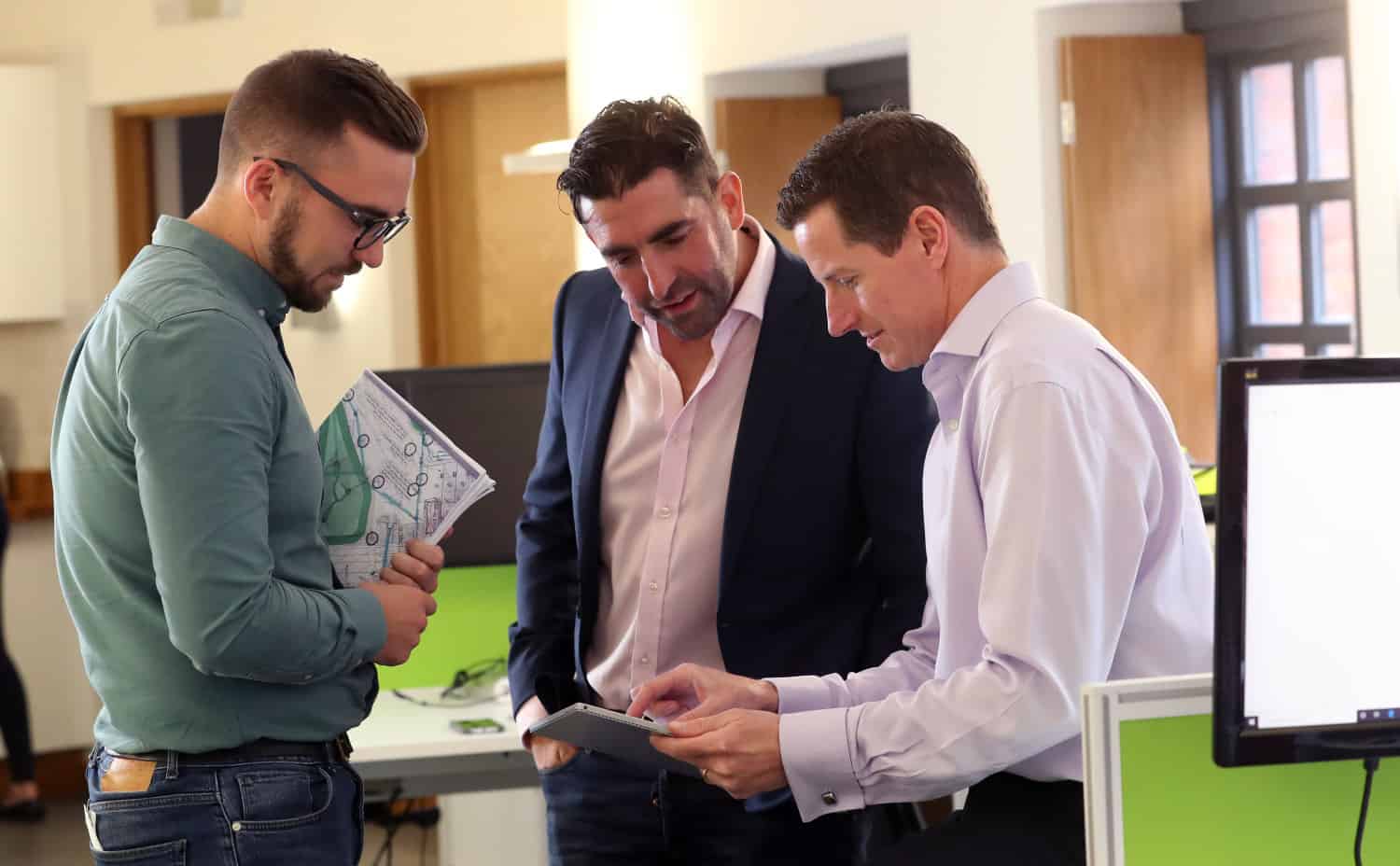 Three men in an office looking at an Ipad discussing designs