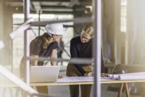 Front view of two women standing by the desk reviewing blueprints.